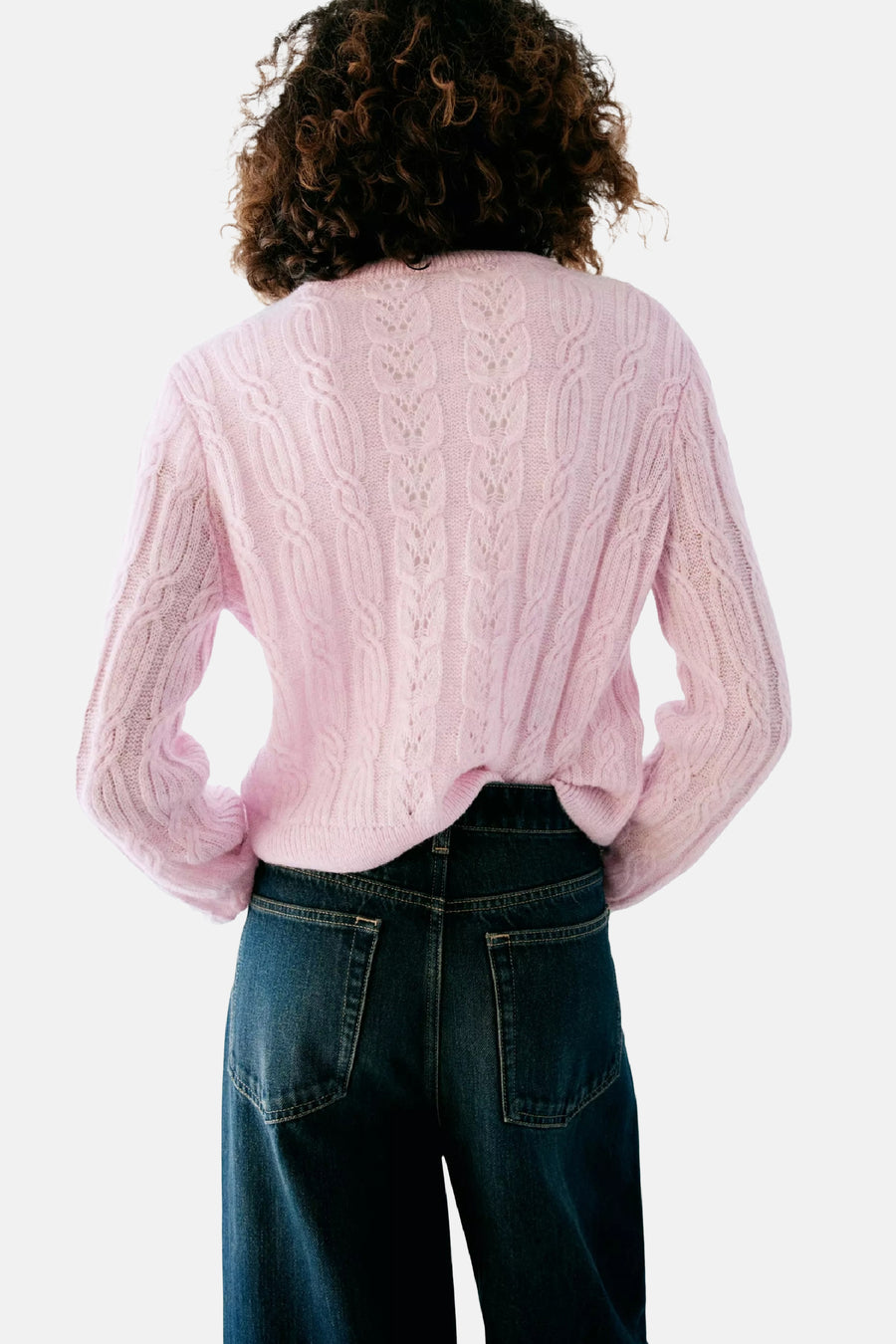 Roze gebreide gilet van MANGO, met kabelpatroon en open rug, achterzijde weergegeven op model in donkerblauwe jeans