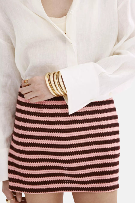 Multicolor gestreepte gebreide rok van MANGO, roze en bruin, met textuur, gedragen met witte blouse en gouden armbanden, close-up.