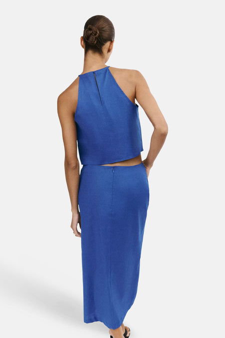 Blauwe mouwloze blouse van MANGO, rugzicht met centrale ritssluiting, gepaard met bijpassende lange rok, model met opgestoken haar.