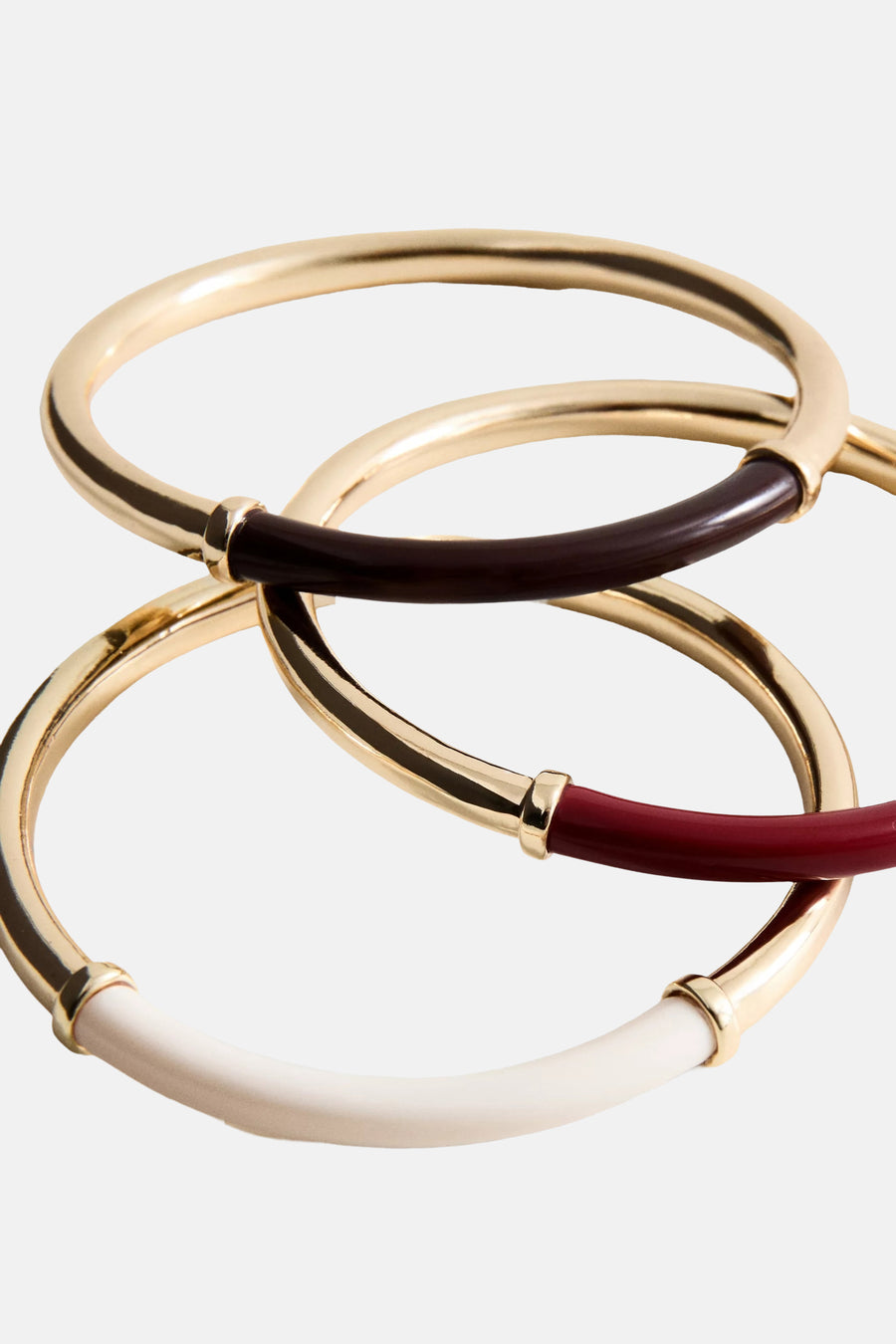 Multicolor armband van goudkleurig metaal met wit, rood en donkerbruin inzetstuk, van MANGO, gestapeld op lichte achtergrond