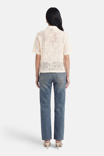 Chemisier beige à manches courtes de Terra di Siena, ajouré à motif floral, vue arrière, porté sur un jean et des talons.