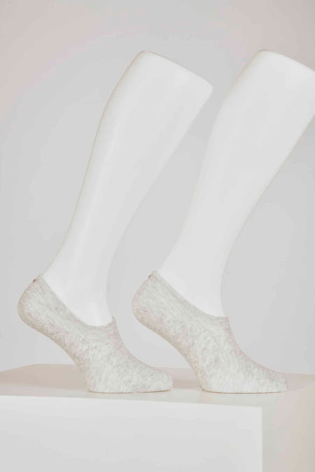 Chaussettes grises de TOMMY JEANS, portées sur des pieds de mannequin blancs, debout sur un sol blanc.