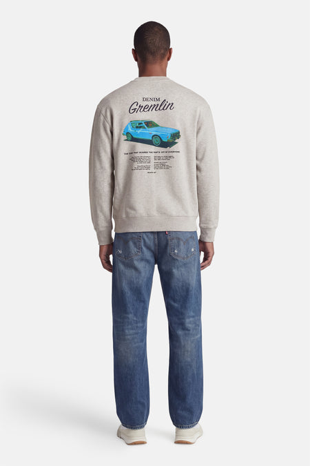 Sweat-shirt gris Levi's® avec une voiture AMC Gremlin bleue et du texte dans le dos, porté par un homme avec un jean bleu et des baskets.