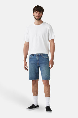 Man in wit T-shirt en denim shorts met zwarte slip-on schoenen.