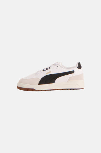Baskets blanches PUMA avec bande d'accent noire et semelle marron, vue de côté.