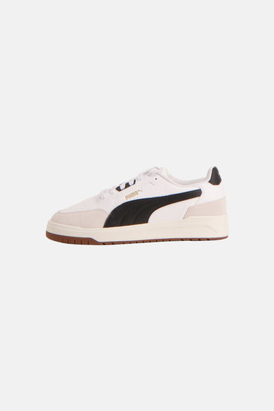 Baskets blanches PUMA avec bande d'accent noire et semelle marron, vue de côté.