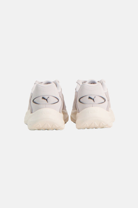 Achteraanzicht van een paar grijze sneakers van PUMA, met crèmekleurige zolen en het logo op de hiel.