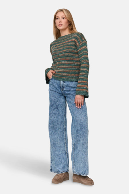 Vrouw draagt gestreepte trui, wijde jeans en suède schoenen.