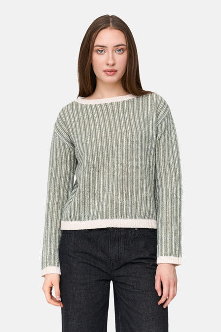 T-shirt vert avec col rond de 24 Colleurs,, des rayures verticales et des manches longues, porté avec un pantalon noir.