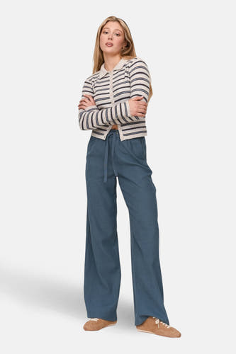 Tunique écru de 24 couleurs GMBH, avec des rayures horizontales, portée avec un pantalon bleu et des chaussures marrons.