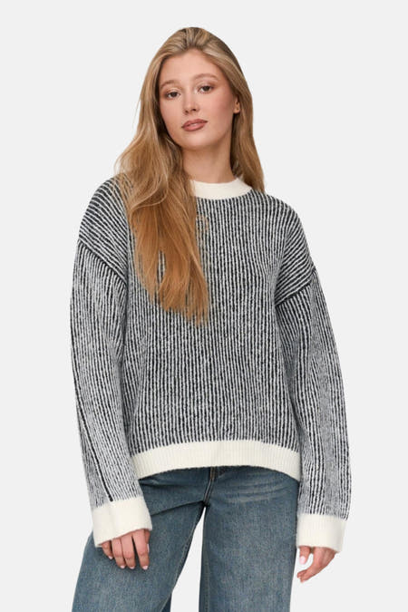 Pull-over noir à col rond de 24 Colleurs, avec un un un motif rayé, combiné avec des jeans.
