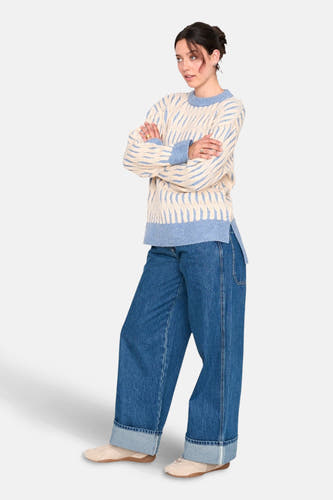 Pull-over bleu rond de cou avec 24 colors gmbh, avec un motif ondulé, combiné à des jeans larges et des baskets.