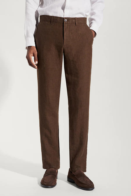 Pantalon de costume brun MANGO, avec une texture subtile et une fermeture à boutons, porté avec un chemisier blanc en lin.