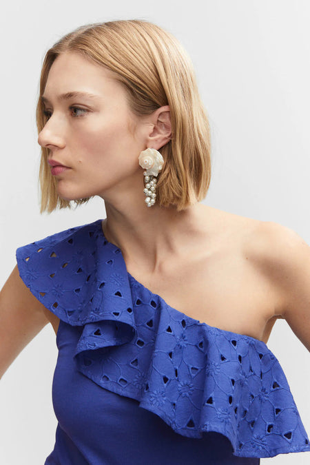 Débardeur bleu avec volants et détail en dentelle de MANGO, design asymétrique, profil latéral d'un modèle portant de grandes boucles d'oreilles