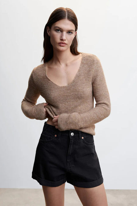 Short noir à 5 poches de MANGO, avec jambes retroussées et poches classiques, porté avec un pull beige dans une photo lifestyle.