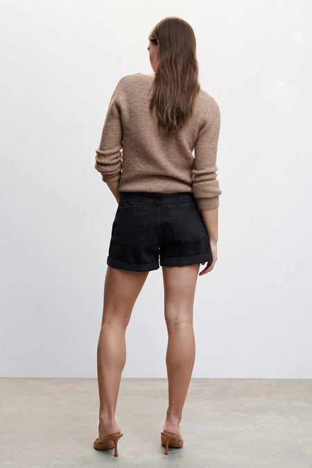 Short noir à 5 poches de MANGO, vue arrière, avec jambes retroussées et pull beige, modèle en talons hauts