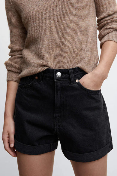 Short noir à 5 poches de MANGO, avec jambes retroussées et bouton argenté, porté avec un pull beige, vue de face.