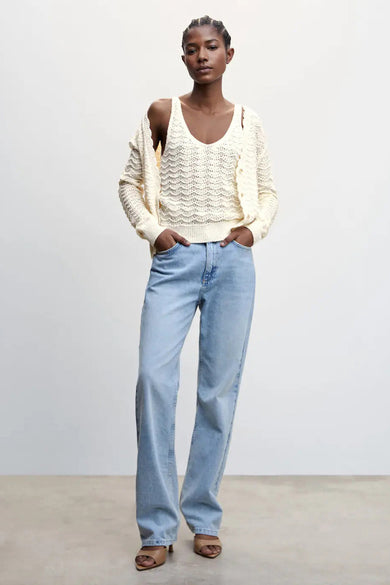 Débardeur beige en maille de MANGO, avec un profond décolleté en V et un motif ajouré, porté sous un cardigan crème, un jean bleu clair et des sandales marron, vue de face.