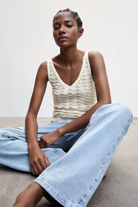 Débardeur beige en maille à col en V de MANGO, porté avec un jean bleu clair, assis dans une pose lifestyle