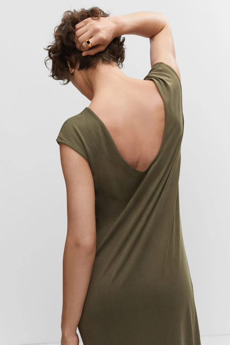 Robe longue beige de MANGO, dos avec un décolleté en V profond, tissu doux, le modèle porte une bague et une boucle d'oreille dorées