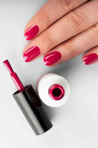 Vernis à ongles en gel fuchsia de Pn Selfcare, avec un flacon ouvert et une main aux ongles vernis.