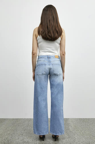 Jean bleu clair large de PULZ, vu du dos, avec un chemisier blanc et des baskets noires.