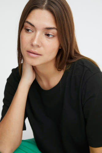 T-shirt noir à manches courtes de PULZ, porté par une femme avec un pantalon vert.