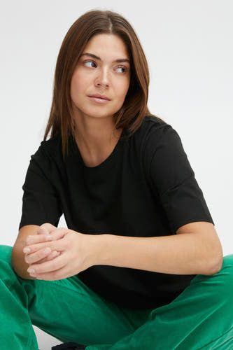 T-shirt noir à manches courtes de PULZ, porté avec un pantalon vert.