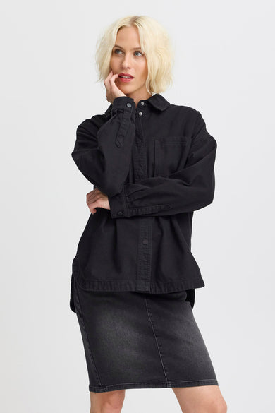 T-shirt de jeans noir PULZ, avec des manches longues et des boutons visibles, porté avec une jupe en jeans.