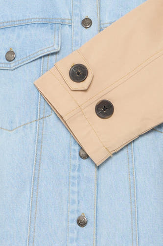 Veste en jeans bleu clair de PULZ, avec des bords de manches beige contrastants et une fermeture à boutons.