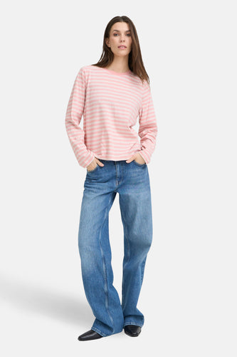 Vrouw in roze gestreept shirt en wijde jeans, staand.
