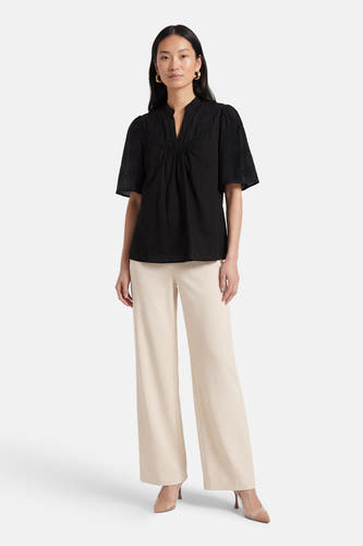 Zwarte blouse met korte mouwen van PULZ, met subtiele details en gecombineerd met beige, wijde broek en hakken.
