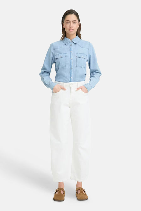 Witte spijkerbroek met speciale pasvorm van PULZ, gedragen door een model met een lichtblauwe spijkerblouse en bruine schoenen.