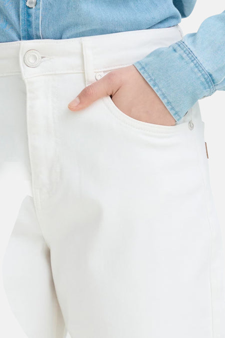 Jean en denim blanc de PULZ, détail avec une main dans la poche avant, bouton argenté et une chemise en jean bleu clair.