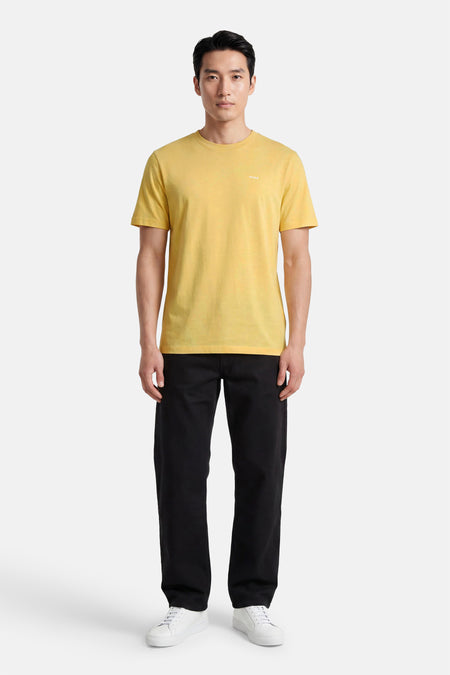 T-shirt jaune à manches courtes de HUGO, avec un petit logo blanc imprimé sur la poitrine, porté par un homme en pantalon noir et baskets blanches.