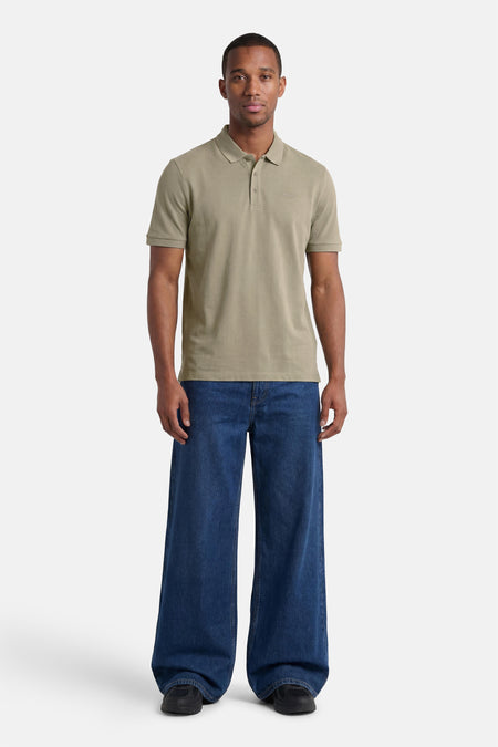 Polo verte HUGO verte de couleur verte avec logo et manches courtes, portée par un homme en jean large bleu foncé et baskets noires.