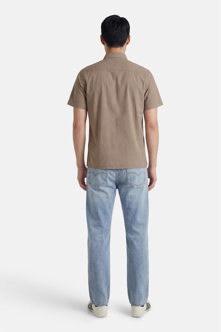 Chemise marron à manches courtes de HUGO, vue de dos, associée à un jean et des baskets blanches.