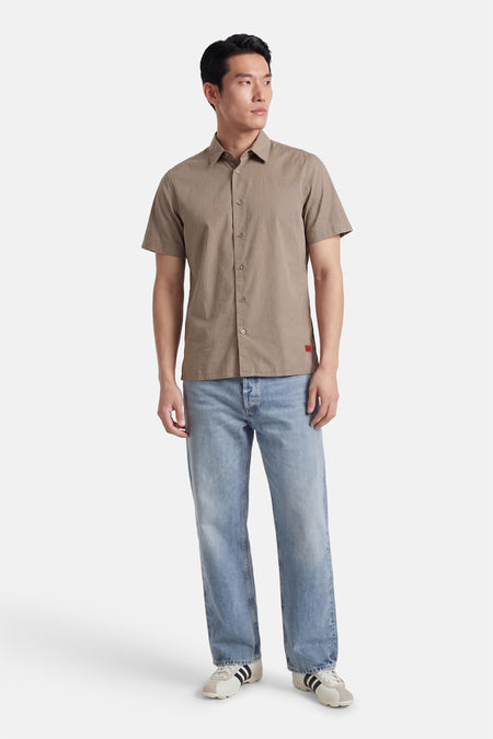 Chemise marron à manches courtes de HUGO, avec fermeture boutonnée, portée avec un jean bleu et des baskets blanches.
