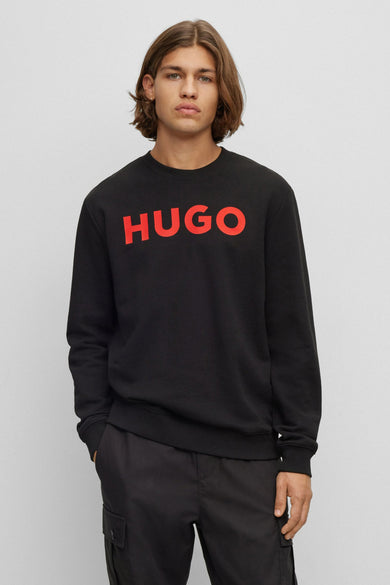 Pull-over noir HUGO, avec le nom de marque rouge sur la poitrine, porté décontracté par un homme.