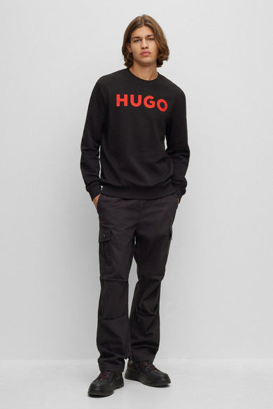 Pull-over noir avec col rond de HUGO, avec logo de la marque rouge sur la partie avant, associé à un pantalon cargo noir et des chaussures.