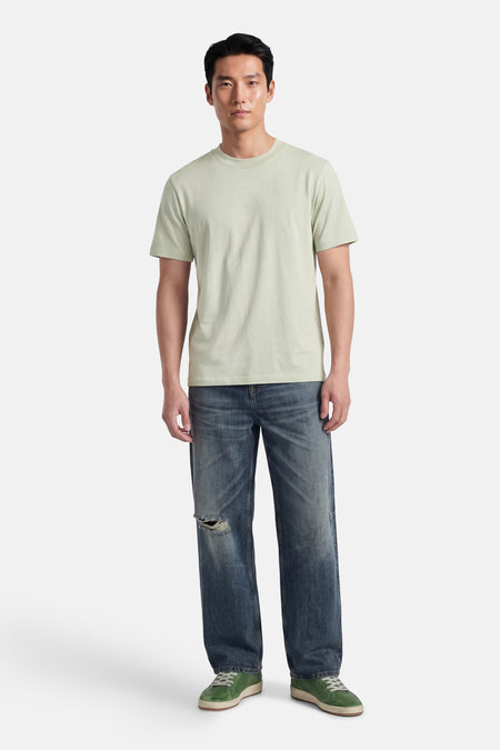 T-shirt vert à manches courtes de HUGO avec un logo discret sur la poitrine, porté par un homme avec un jean déchiré et des baskets vertes.