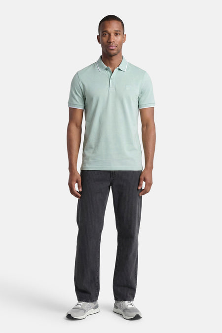 Polo turquoise HUGO BOSS ORANGE avec passepoil blanc sur le col et les manches, porté par un homme avec un pantalon foncé et des baskets grises.