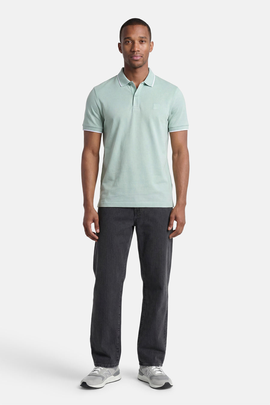 Polo turquoise HUGO BOSS ORANGE avec passepoil blanc sur le col et les manches, porté par un homme avec un pantalon foncé et des baskets grises.