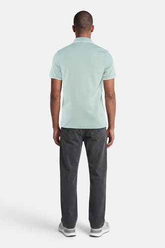 Polo turquoise HUGO BOSS ORANGE avec passepoil blanc au col et aux manches, arrière sur homme avec jean foncé et baskets grises.