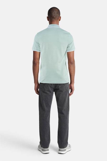 Polo turquoise HUGO BOSS ORANGE avec passepoil blanc au col et aux manches, arrière sur homme avec jean foncé et baskets grises.