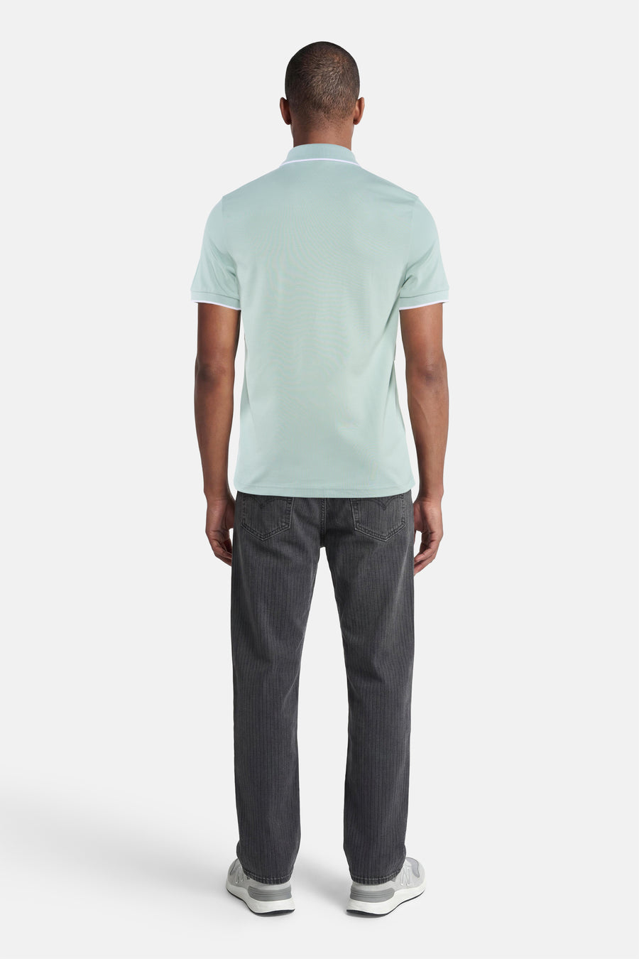 Polo turquoise HUGO BOSS ORANGE avec passepoil blanc au col et aux manches, arrière sur homme avec jean foncé et baskets grises.