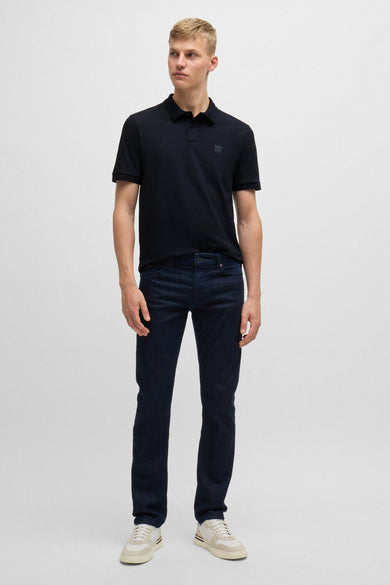 Man in marineblauwe polo, jeans en witte sneakers.