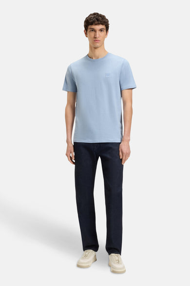 T-shirt bleu à manches courtes de HUGO BOSS, porté avec des jeans foncés et des baskets crème.