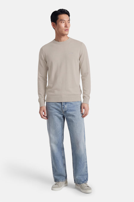 Pull gris à col rond de HUGO BOSS ORANGE, porté avec un jean bleu et des baskets en daim.