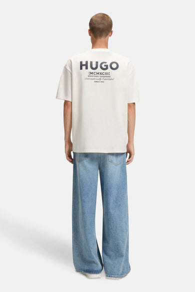 Achterkant van een man die een crèmekleurig HUGO T-shirt en wijde blauwe jeans draagt.